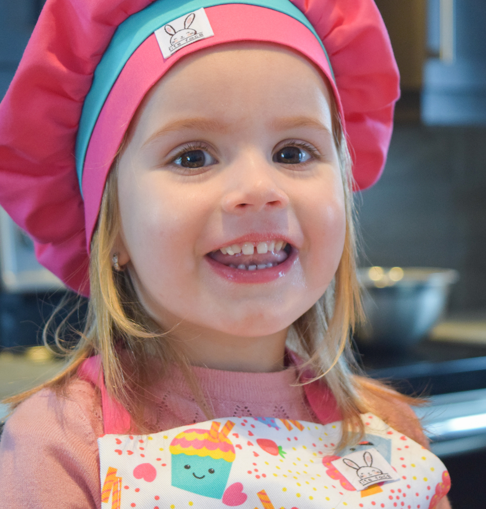 Une petite fille porte le chapeau de chef de couleur fuchsia. Il est ajustable à l'aide d'un élastique. Fabriqué au Québec. Taille unique.