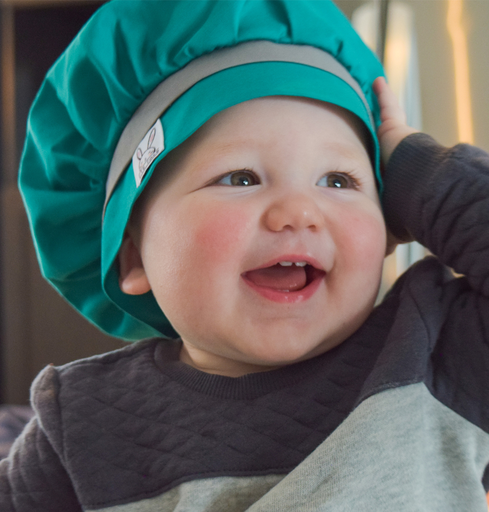 Un petit garçon porte un chapeau de cuisine de couleur émeraude qui s'ajuste pour toutes les têtes d'enfants. Fabriqué au Québec. Taille unique.