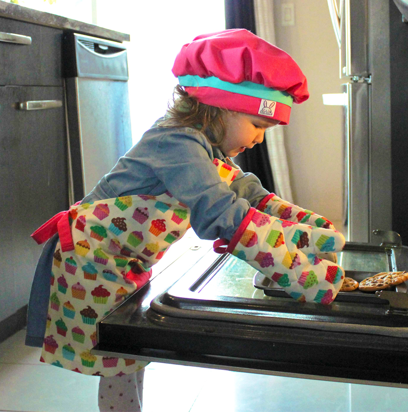 Petite fille portant un ensemble de cuisine; tablier, mitaines de four et chapeau de chef.