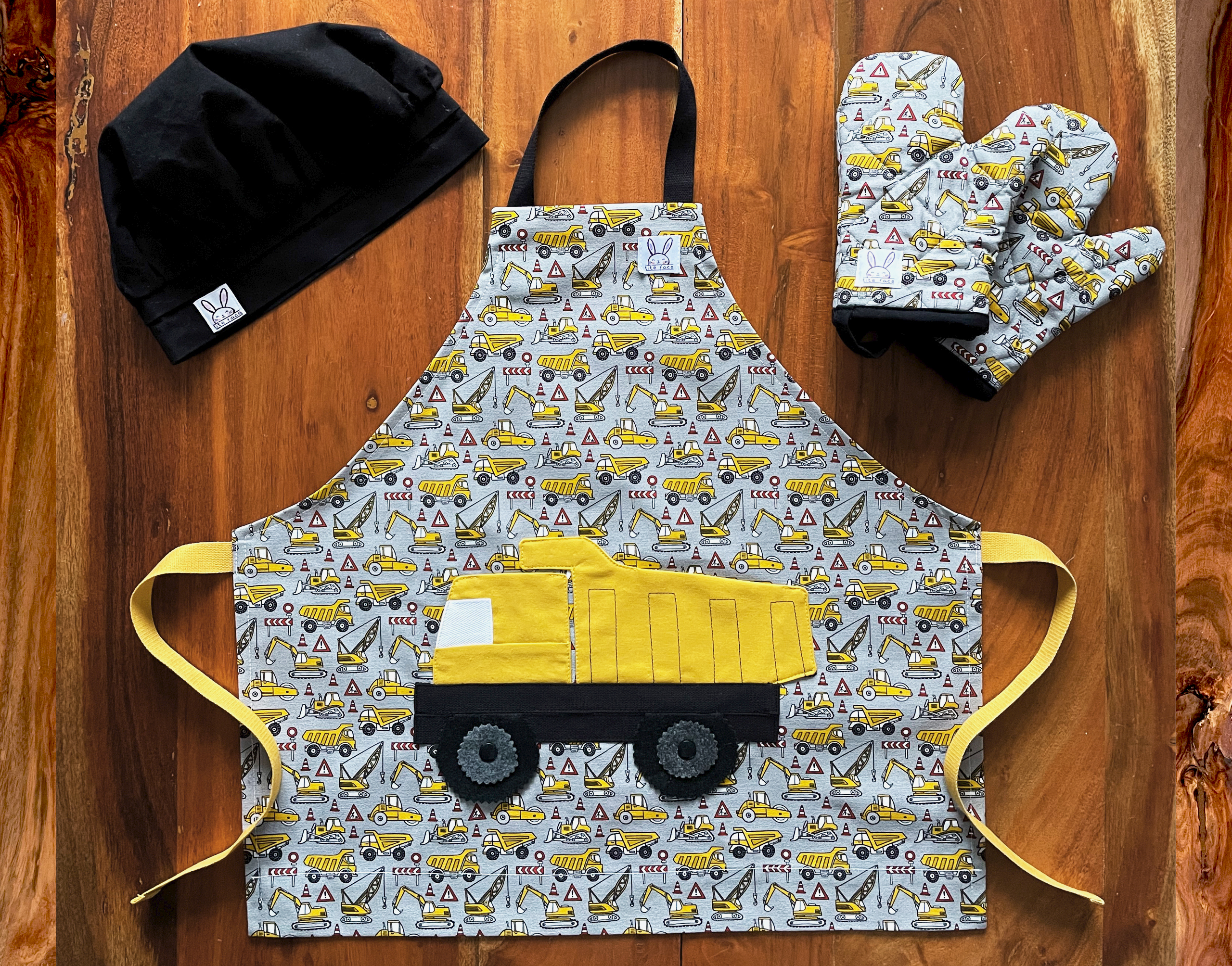 Ensemble de ''mini-chef'' pour faire fureur dans la cuisine ! Le tout comprend: 1 tablier, 1 paire de mitaine et 1 chapeau ajustable. Le tablier s'ajuste à l'encolure à l'aide de boutons pressions. 2 poches amusantes au devant en forme de camion. Mitaines de four isolées à double épaisseur. Ganse pour accrocher les mitaines sur un crochet. Le Chapeau de cuisine est ajustable et confortable à l'aide d'un élastique. Fabriqué au Québec.