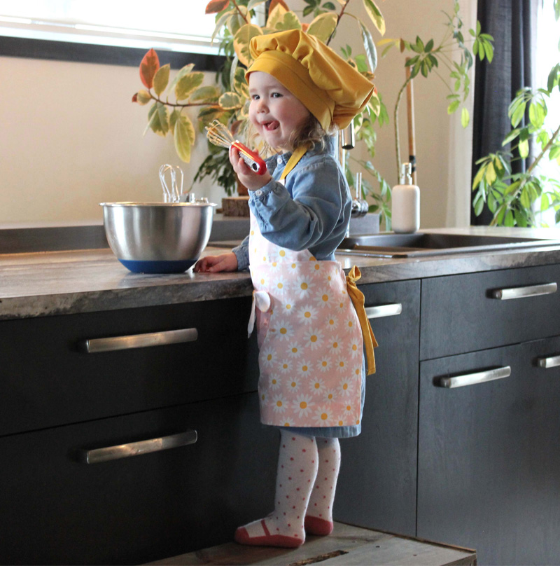Une petite fille qui prépare une recette. Elle porte un petit tablier fleuri rose et jaune. Le petit chapeau de chef jaune qui s'agence au tablier. Une vrai petite chef!