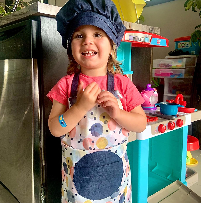 Une petit fille qui s'amuse avec sa cuisinette. Elle porte un petit tablier à pois ainsi qu'un chapeau de chef en denim pour bien jouer son rôle.